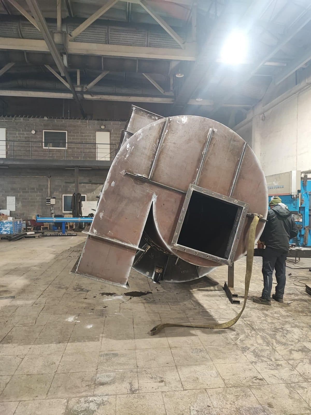 Round welded steel hood with a square opening, standing in the workshop