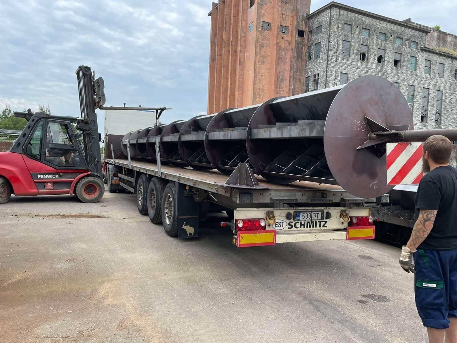 Long steel screw conveyor loaded on a Schmitz flatbed, a forklift beside it
