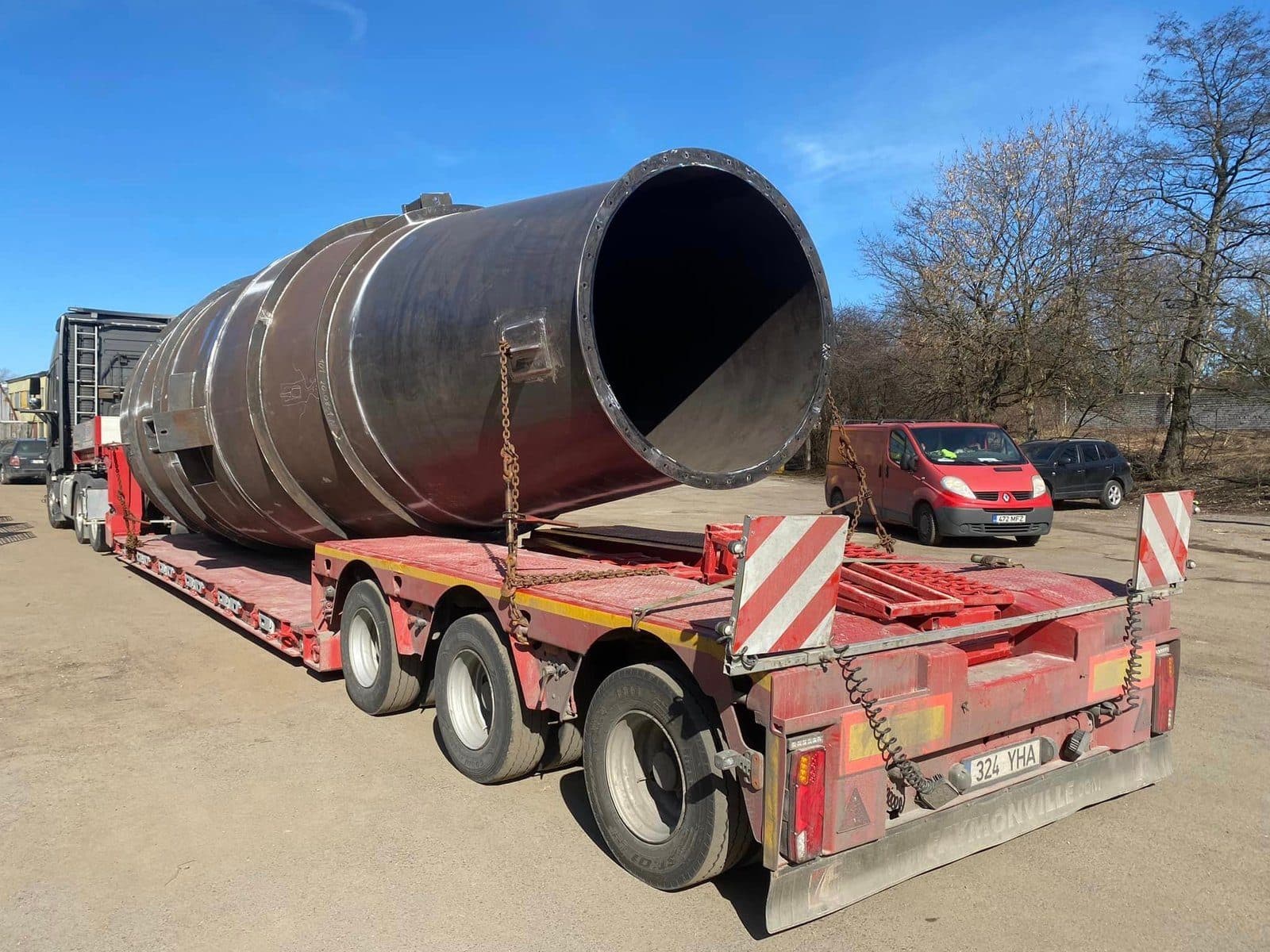 Large rolled steel cylinder chained down on a red low-loader trailer