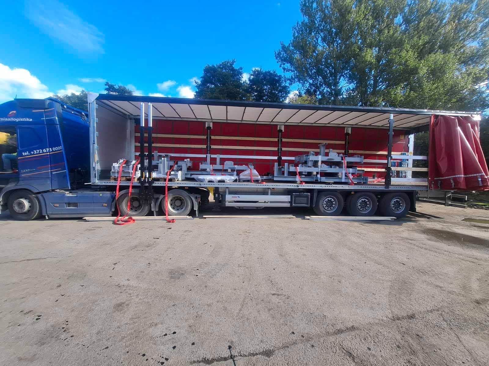 Curtainsider trailer with red curtains open, loaded with light steel frames at the Novatex yard in Tallinn